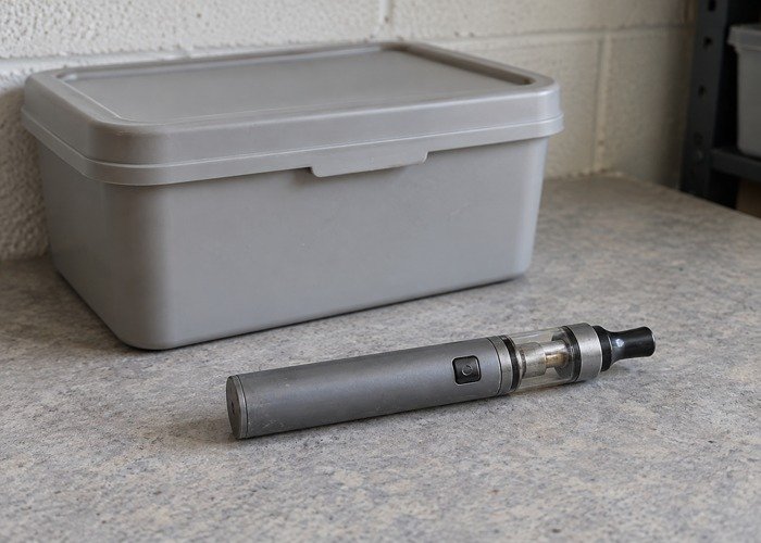 Intact unbranded discarded e-cigarette beside a closed storage container